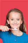 Portrait of girl holding toothbrush against red background