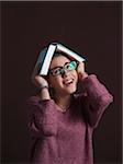 Portrait of Teenage Girl wearing Eyeglasses, holding Open Book over Head with Anxious Expression, Studio Shot on Black Background