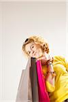 Low Angle View Portrait of Blond Teenage Girl with Curly Hair, holding Shopping Bags and Smiling at Camera, Studio Shot on White Background