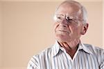 Portrait of Senior Man wearing Aviator Eyeglasses and Looking up into the Distance with Confident Expression in Studio on Beige Background