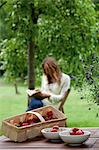 Fraises sur table de jardin, jeune femme lisant dans le dos