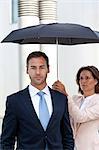 Businesswoman holding umbrella above businessman