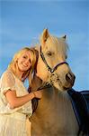 Femme souriante en robe blanche avec cheval sous le ciel bleu