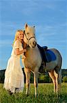 Lächelnde Frau in weißen Kleid mit Pferd auf der Wiese