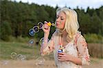 Happy young blond woman blowing soap bubbles outdoors