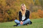 Souriant blonde jeune femme assise au pré automnal