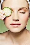 Woman covering eye with piece of cucumber