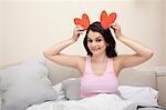 Woman in bed holding heart shapes as ears