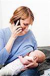 Mother on phone breast feeding newborn daughter