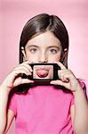 Girl holding smartphone over mouth, sticking out tongue