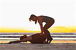 Instructor helping woman into yoga pose on beach