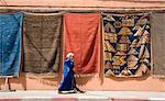 Une femme en robe islamique à pied par un mur accroché avec des tapis dans la médina de Marrakech, au Maroc, en Afrique du Nord, Afrique