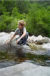 Boy Sitting on Rock by River