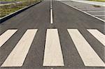 Perspective of an asphalt road with crosswalk stripes in the foreground