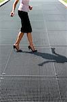 cropped view of mid adult business woman walking on high heels, trying to balance on grating