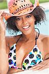 A beautiful sexy young African American girl or young woman wearing a bikini and straw cowboy hat laughing on the side of a swimming pool.