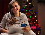 Smiling woman with tablet PC and credit card in front of Christmas tree