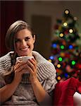 Happy young woman with cup of hot chocolate in front of Christmas lights