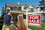 Young Family Looking at a Beautiful New Home with a For Sale Real Estate Sign in Front.