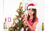 Beautiful Asian woman decorating Christmas tree in her house