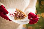 Woman Wearing A Sweater and Seasonal Red Mittens Holding A Plate of Pecan Pie with Peppermint Sticks.