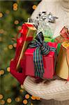 Woman Wearing A Sweater and Seasonal Red Mittens Against an Abstract Green and Golden Background Holding Beautifully Wrapped Christmas Gifts.