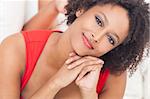 A beautiful mixed race African American girl or young woman laying down on a sofa wearing a red dress looking happy