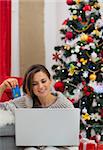 Smiling woman with laptop and credit card sitting near Christmas tree
