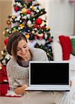 Happy woman looking laptop blank screen near Christmas tree