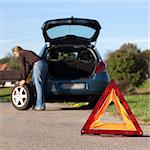 Changing the tire on a broken down car on a road with red warning triangle