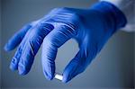 Hand in blue surgical glove holding capsule