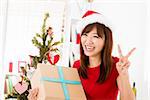 Excited Asian woman getting her Christmas present, showing peace hand sign, indoor/inside her home.