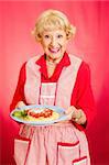 Sweet retro grandmother holding a plate of fresh, hot Italian Spaghetti with marinara sauce.  Red background.