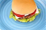 Mini cheese burger with tomato and lettuce on a blue dish. With copy space.