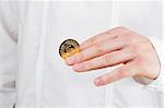 Close-up photograph of a golden coin between a man's fingers.