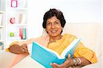 Mature 50s Indian woman reading a book at home