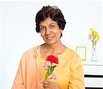 Portrait of a mature Indian woman holding carnation flower at home