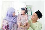 Southeast Asian family. Muslim girl hand holding money jar at home.