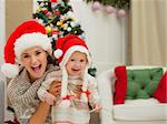 Portrait of mom and eat smeared baby girl in Christmas hats near Christmas tree