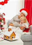 Closeup on Christmas Gingerbread house and mother and baby girl using tablet PC in background