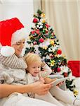 Happy mother and kid using tablet PC near Christmas tree