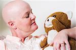Cancer patient, bald from chemotherapy, gets comfort from holding a stuffed teddy bear.