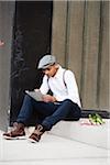 Portrait of Man Sitting on Step with Flowers, Using a Tablet, Mannheim, Baden-Wurttemberg, Germany