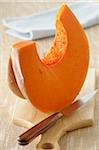 Close-up of Wedge of Pumpkin on Cutting board with Knife on Beige Background, Studio Shot