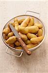 Overhead View of Potatoes in Colander with Knife on Beige Background, Studio Shot