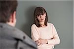 Portrait of Young Woman Standing in front of Young Man, Looking at him Intensely, Studio Shot on Grey Background