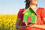 Woman holding model house in field