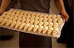 A person holding a baking tray of unbaked croissants