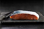 Fresh salmon fillet with skin on a chopping board with a knife