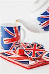 Tea being poured from a Union Jack teapot with matching cupcakes